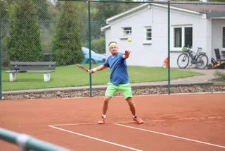 Ein Junge schlägt den Ball, dahinter das Vereinsheim