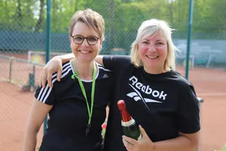 Zwei Mitglieder mit einer Flasche Sekt auf dem Platz
