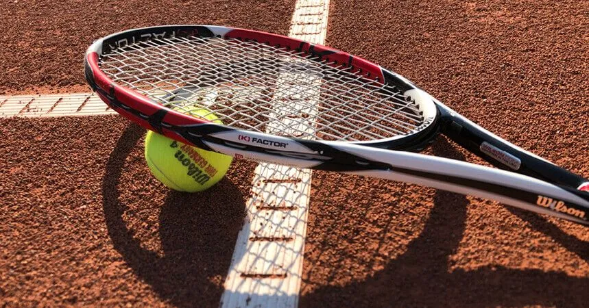 Ein Tennisschläger mit Ball auf der Linie des Sandplatzes