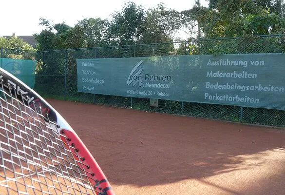 Werbebanden am Zaun der Anlage, davor ein Tennisschläger